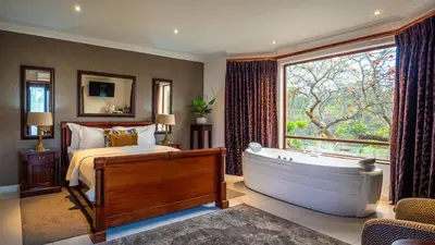 a bedroom with a tub and a bed with a window at Indalo Leaves Lodge and Spa in Nelspruit