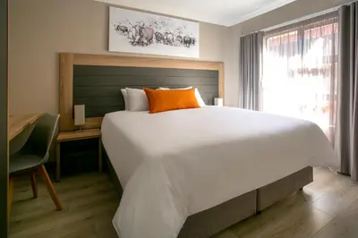 a bedroom with a large white bed and a desk at Hotel AT Hatfield Apartments in Pretoria