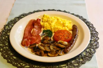 a plate of breakfast food with sausage eggs mushrooms and tomatoes at Kaia Tani Exclusive Guesthouse in Phalaborwa