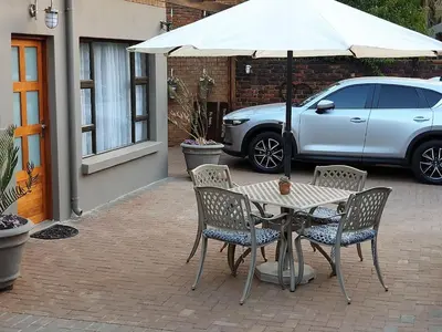 a table and chairs with an umbrella and a car at @Home in the East in Pretoria