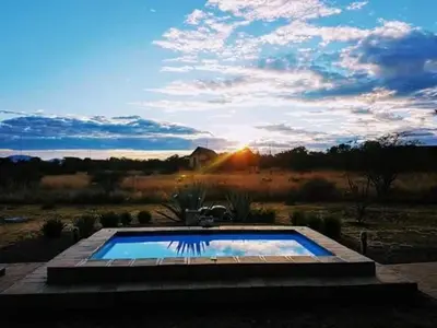 a swimming pool in the middle of a field with the sunset at Zebula - HT1 - 5 Bedroom Holiday Home in Mabula