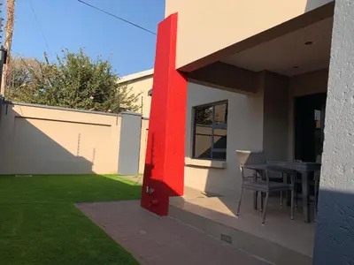 a house with a red wall and a table on the porch at 66 Dorp Street Apartment in Polokwane