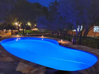 a blue swimming pool at night with lights at Golden Impalas Bush Resort in Hammanskraal