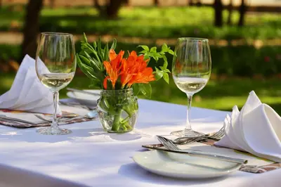 a table with two wine glasses and a vase with orange flowers at Golden Impalas Bush Resort in Hammanskraal