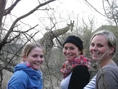 three women are standing in front of a giraffe at Kruger Inn Backpackers in Marloth Park