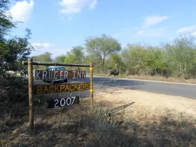 a sign on the side of a road with an ostrich behind it at Kruger Inn Backpackers in Marloth Park