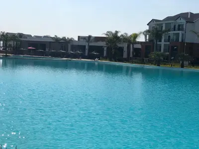 a swimming pool with blue water in front of houses at A Coastal/island experience at a Large 2 bed apartment at a Crystal Lagoon Estate. in Pretoria