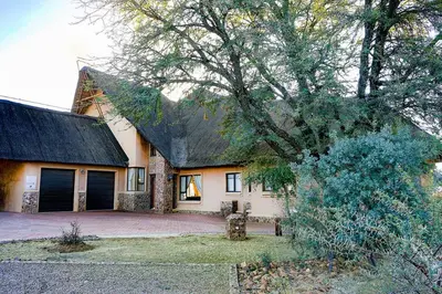 a house with a black roof and a tree at Zebula 8 Bedroom Lodge – IV1 in Mabula