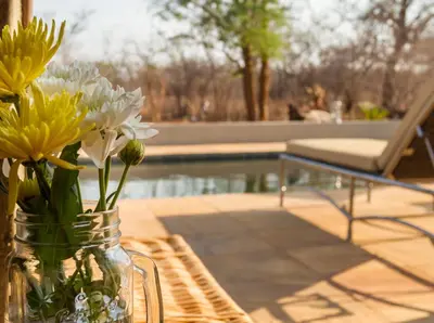 a glass jar filled with yellow and white flowers on a table at Ukuthula Bush Lodge in Hoedspruit