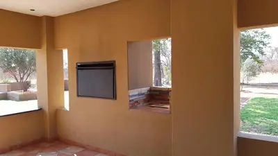 a room with a tv on a wall with two windows at Hornbills Rest Country Home in Phalaborwa