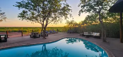 a pool on a deck with tables and couches next to at Mopane Bush Lodge in Linton