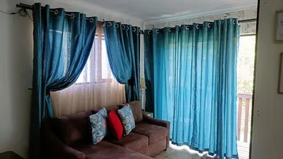 a living room with blue curtains and a brown couch at King Protea Self Catering Accommodation in Erasmuskloof, Pretoria East in Pretoria