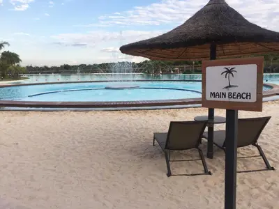 a sign in front of a swimming pool with two chairs and an umbrella at The Blyde - Beachfront in Pretoria