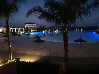 a swimming pool at night with umbrellas and palm trees at The Blyde - Beachfront in Pretoria