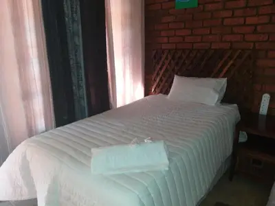 a white bed in a bedroom with a brick wall at Home Sweet Home in Polokwane