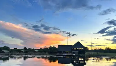 a building on the water with a sunset in the background at Little Mongena Tented Camp in Klipdrift