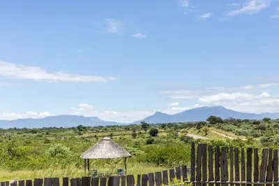 a table and chair in a field with mountains in the background at Hornbills lodge bnb in Mbabat