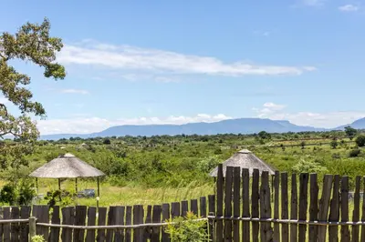 a fence with a view of a field and mountains at Hornbills lodge bnb in Mbabat