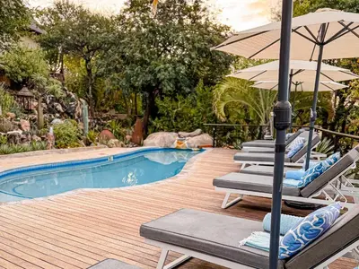 a group of chairs and an umbrella next to a pool at The Wild Blue Lodge SAFARI & SPA in Hoedspruit