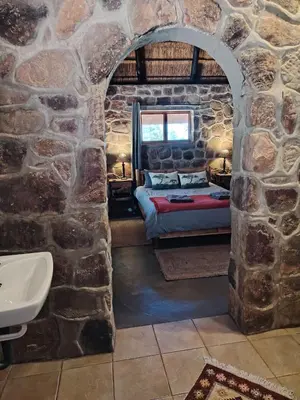 a stone walled bedroom with a bed and a sink at Cross Pollination Chalets & Camping in Vaalwater