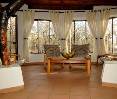 a living room with a table and chairs and windows at Chip n Debs Kruger Vacations in Marloth Park