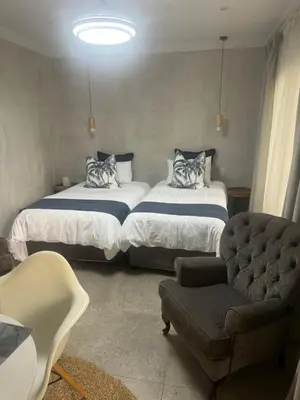 two beds in a room with a chair and a couch at Annie’s Place Self Catering 2 in Kempton Park