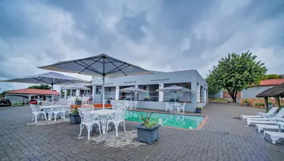 a patio with white chairs and tables and umbrellas at Khayalami Hotel - Emalahleni in Witbank