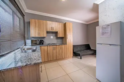 a kitchen with wooden cabinets and a white refrigerator at Khayalami Hotel - Emalahleni in Witbank