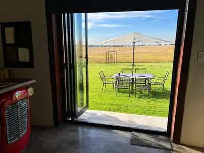an open door with a table and chairs and an umbrella at Merino Stal Guest Farm in Ermelo