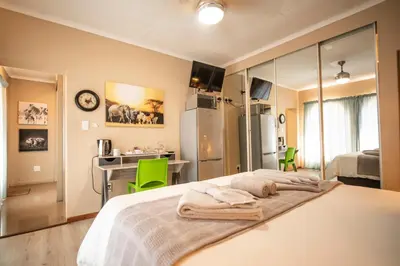 a bedroom with a bed and a desk and a kitchen at Meadowbrook Guesthouse in Pretoria