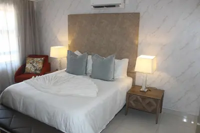 a bedroom with a white bed with two lamps and a chair at Prisatt Boutique Hotel in Onverwacht