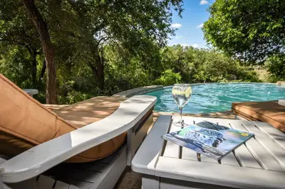 a table with a glass of wine next to a swimming pool at Leopard's Lair Bush Lodge in Hoedspruit