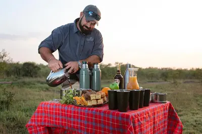 a man is standing next to a table with food at Thabamati Luxury Tented Camp in Timbavati Game Reserve