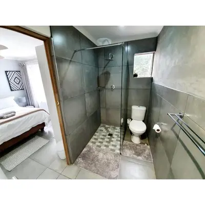 a bathroom with a shower with a toilet and a bed at Waterfall Bed & Breakfast in Midrand