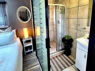 a bathroom with a shower next to a bed and a sink at URlyfstyle Cottage 10km from OR Tambo Int Airport in Kempton Park