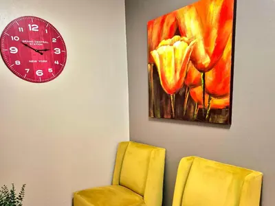 a room with a clock and a chair and a flower painting at URlyfstyle Cottage 10km from OR Tambo Int Airport in Kempton Park