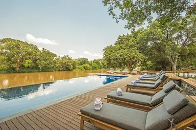 a row of lounge chairs on a wooden deck next to a river at Abelana River Lodge in Phalaborwa