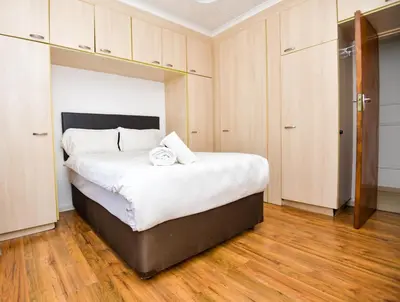 a bedroom with a bed with white sheets and wooden floors at Spacious Menlyn Maine Villa in Pretoria