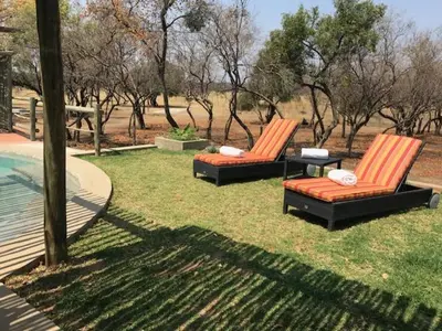 two chairs sitting in the grass next to a pool at Kareefontein 8 Bedroom Lodge IKH1 in Mabula