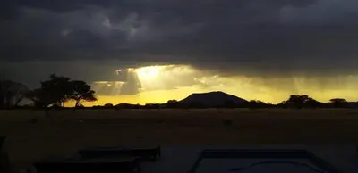 a stormy sky with the sun shining behind a mountain at Kareefontein 8 Bedroom Lodge IKH1 in Mabula