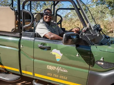 a man sitting in the door of a green jeep at Buffalo Rock Tented Camp in Hazyview