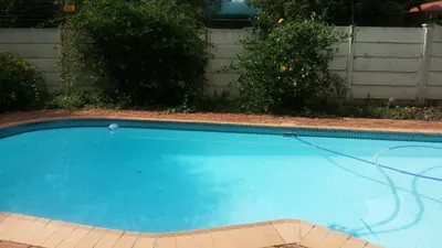 a blue swimming pool with a cord in a yard at Chariots Guest House in Polokwane