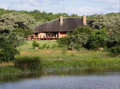 a house with a black roof next to a lake at Metsi Lodge in Welgevonden Game Reserve