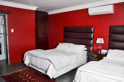 two beds in a room with a red wall at Casa de Ross in Pretoria