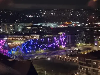 a city at night with a blue and purple bridge at The Capital Trilogy Menlyn Maine in Pretoria