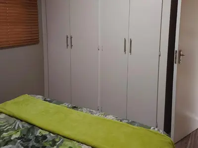 a bedroom with white cabinets and a green blanket on a bed at Sarah's Place Guesthouse in Pretoria