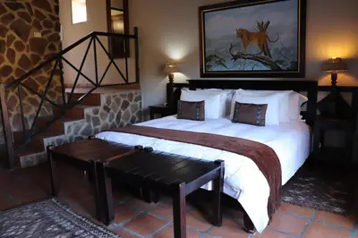 a bedroom with a large bed with a bench next to it at Schrikkloof Private Nature Reserve, home of The Lions Foundation in Bela-Bela