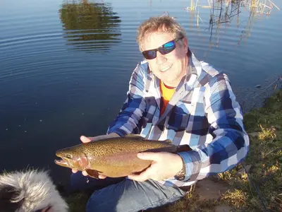 a man sitting in the water holding a fish at Moonlight Meadows just outside Dullstoom in Dullstroom