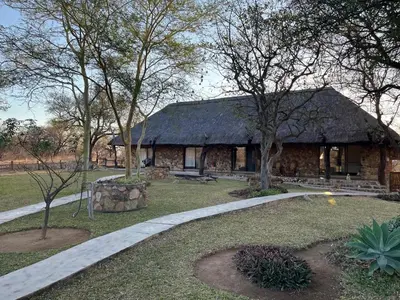 a stone house with a thatched roof with a path leading to it at No 43 - The Eco Lodge in Hoedspruit