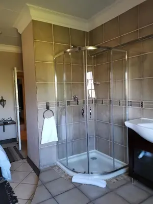 a shower with a glass door next to a sink at Klyne Jiweel Guesthouse in Pretoria